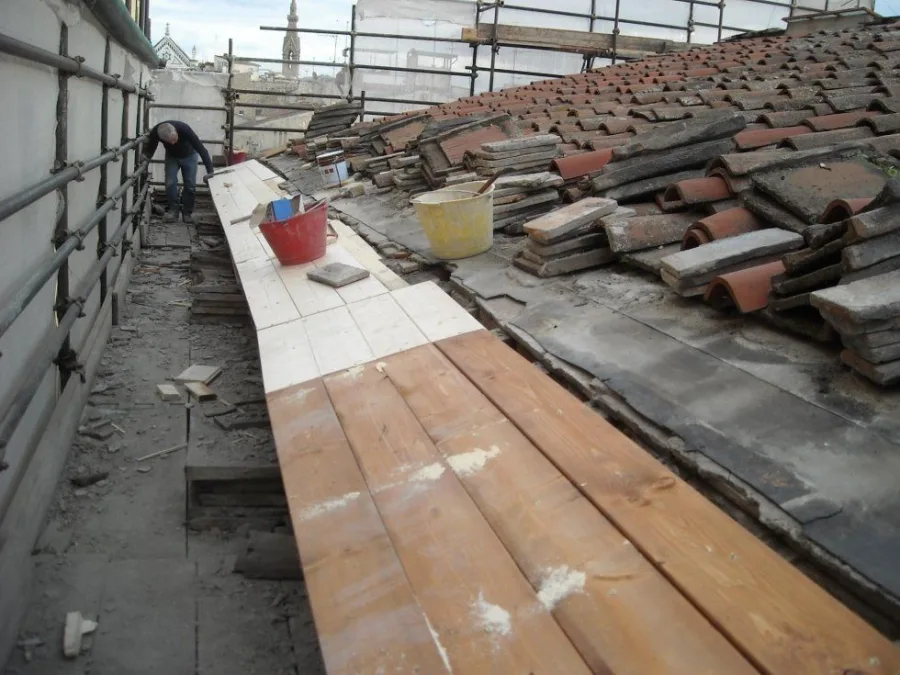 Toiture d'un immeuble ancien en cours de réfection : à droite, vieilles tuiles canal et tuiles plates déposées et empilées en tas sur le rampant décoiffé ; à gauche.
