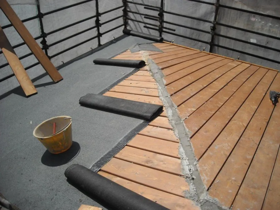 Terrasse / toiture-terrasse en cours d'étanchéité : trois rouleaux de membrane bitumineuse noire partiellement déroulés sur le support gris.