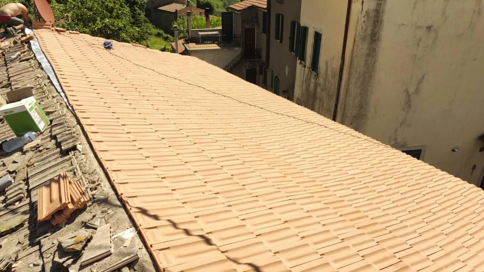 Vue depuis le faîtage d'un long pan de toiture entièrement recouvert de tuiles terre cuite neuves (chantier en cours). À gauche, le pan voisin encore décoiffé avec gravats.